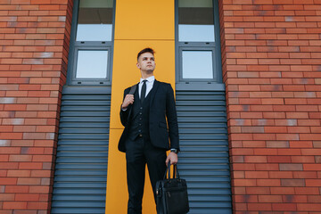Against a backdrop of modern office buildings, a young Caucasian American man in a business suit portrays the image of a professional and driven entrepreneur.