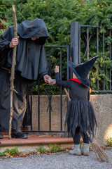A girl dressed as a witch with a hat and a broom, a man in a monk's robe with a staff handing out...