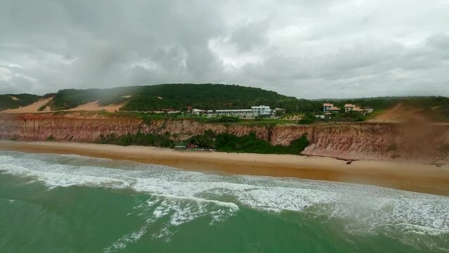 Aerial Forward Shot Of Tourist Resort On Cliff At Beach Near Hill Against Cloudy Sky - Pipa Beach, Brazil
