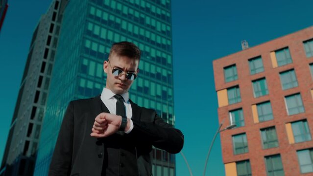 professional white collar worker observing his wristwatch against an urban backdrop, emphasizing punctuality and dedication to work.
