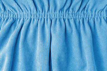 Blue corduroy fabric gathered with elastic close up. Velveteen texture with folds and drapery....
