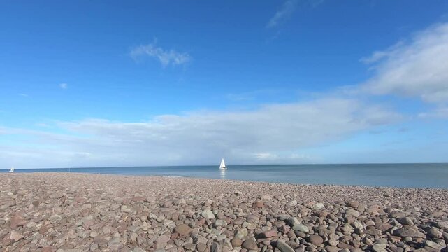 white boat moving on porlock weir sea with stoney beach view in a sunny weather