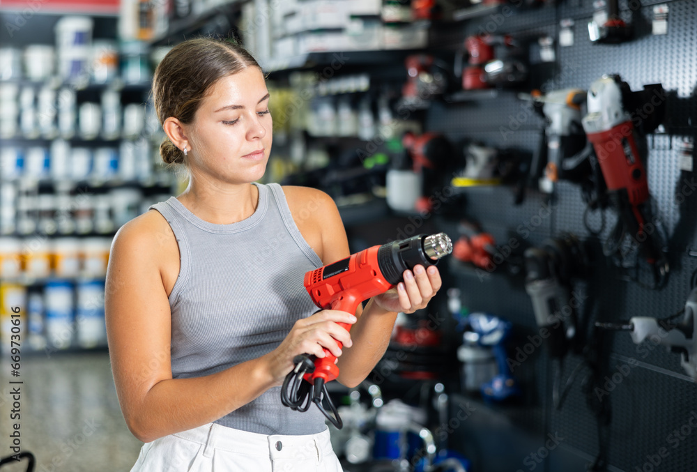 Wall mural Beautiful young woman chooses and buys industrial hair dryer in local hardware store