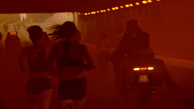 Group of girls running in Paris during a competition and getting through a tunnel with orange fume