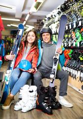 Portrait of smiling woman and man in ski equipment who is standing with ski, helmets and boots in...