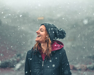 mulher com touca de lã e mãos levantadas, sorrindo, em cenário de inverno com neve caindo 