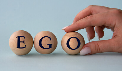 A woman's hand holds a wooden ball with the abbreviation EGO - obrazy, fototapety, plakaty