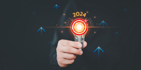 Businessman holding a light bulb with goal icon and the year 2024. Concept of 2024 business planning and strategy innovative business vision and new year resolution target, save energy efficiency. - obrazy, fototapety, plakaty