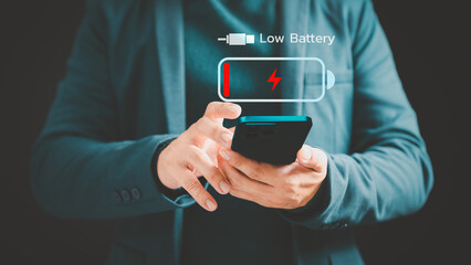 Adult man holding a smartphone with low battery icon on virtual screen. Concept of Technology and daily life. Mobile phone out of battery.