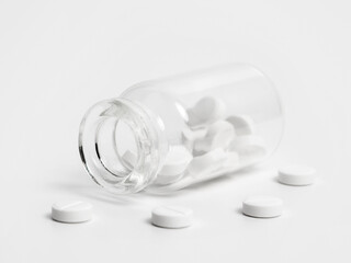 White pills near lying opened glass bottle isolated on white background. Concept of medical...