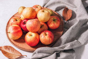 Fresh ripe apples on wooden tray, autumn leaves and grey napkin on white table. Autumn harvest, Thanksgiving concept. Top view