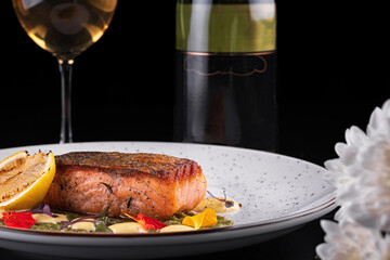 salmon steak in a plate with lemon, on the background of a bottle of white wine and a glass of wine
