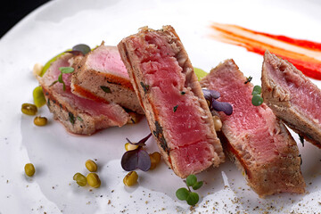 Grilled tuna with capers, on a white plate, on a dark background