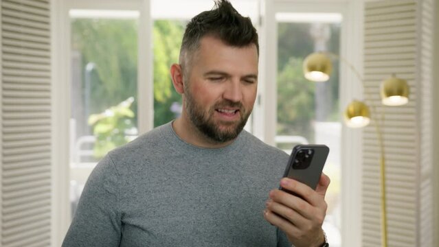 Casual handsome businessman singing and dancing while listening music on smartphone. Cool guy scrolling news or social media on phone in modern light design apartment interior 4K Cinematic RED camera