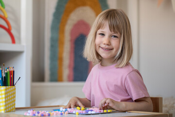 A cute girl makes crafts sitting at a table in the children's room. Development and preschool education.