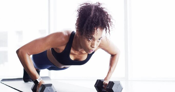Woman, pushups and dumbbell for workout at gym, strong core and endurance training for body. Female person, sweat and exercise for muscle and health, commitment and motivation in fitness by equipment