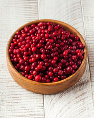Juicy fresh cranberries in a wooden bowl on a white wooden background. Berries.