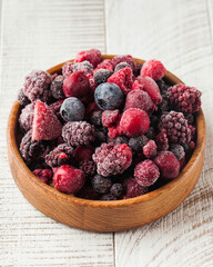 Frozen assorted berries in a wooden bowl on a white background. Berries, frozen foods.