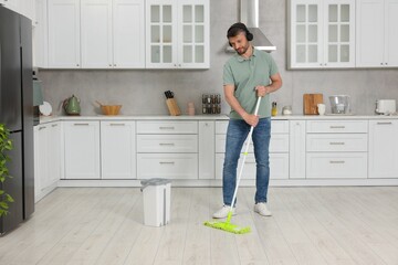 Fototapeta na wymiar Enjoying cleaning. Man in headphones listening to music and mopping floor in kitchen