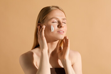 Beautiful young woman with sun protection cream on her face against beige background
