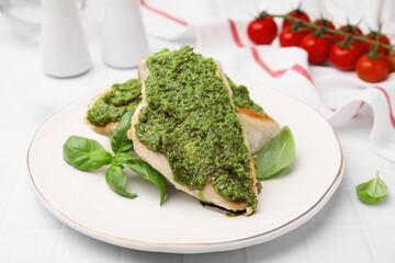 Delicious chicken breasts with pesto sauce and basil on white tiled table