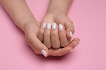 Woman showing her manicured hands with white nail polish on pink background, closeup