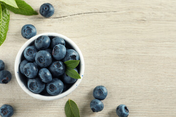 Bowl of fresh tasty blueberries with leaves on white wooden table, flat lay. Space for text