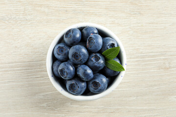 Bowl of fresh tasty blueberries on white wooden table, top view