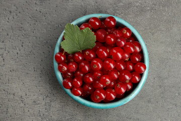 Ripe red currants and leaf in bowl on dark textured table, top view