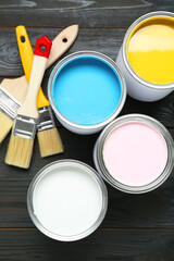 Cans of colorful paints and brushes on black wooden table, flat lay