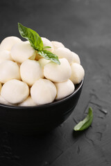 Tasty mozzarella balls and basil leaves in bowl on black table, closeup