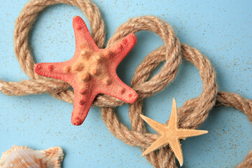 Beautiful sea stars, rope and sand on light blue background, flat lay