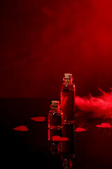 Bottles of love potion, paper hearts and feather on mirror surface against dark background, space...