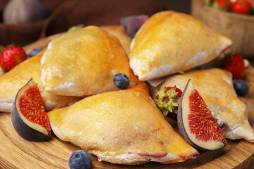 Delicious samosas with figs and berries on wooden board, closeup