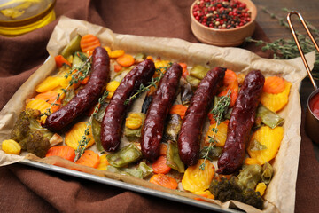 Baking tray with delicious smoked sausages and vegetables on table, closeup