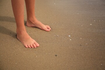Fototapeta na wymiar Little girl standing on sandy beach near sea, closeup. Space for text
