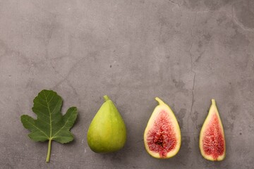 Cut and whole green figs with leaf on light gray table, flat lay. Space for text