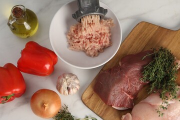 Metal meat grinder with chicken mince and products on white marble table, flat lay