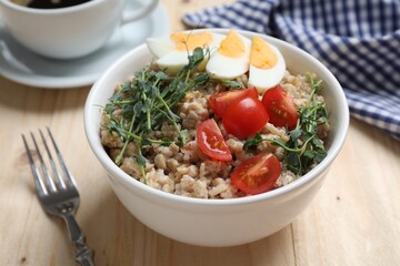 Tasty boiled oatmeal with egg and tomatoes served on wooden table, closeup