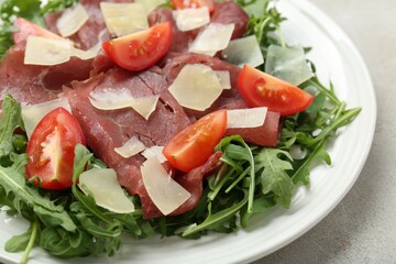 Delicious bresaola salad with parmesan cheese on light grey textured table, closeup