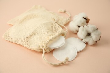 Fototapeta na wymiar Bags with cotton pads and flowers on beige background, closeup