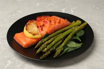 Tasty grilled salmon with tomatoes, lemon and asparagus on grey table