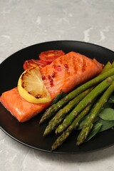 Tasty grilled salmon with tomatoes, lemon and asparagus on grey table