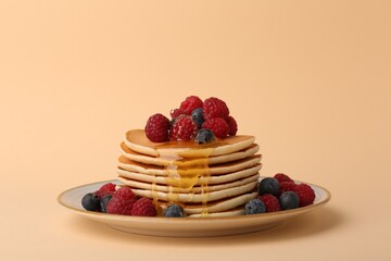 Stack of tasty pancakes with raspberries, blueberries and honey on pale orange background