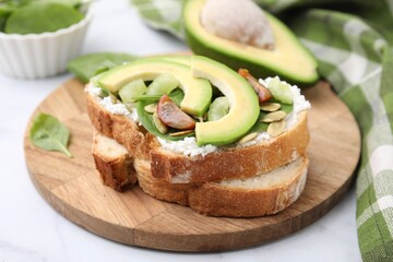 Tasty vegan sandwich with avocado, tomato and spinach on white marble table, closeup