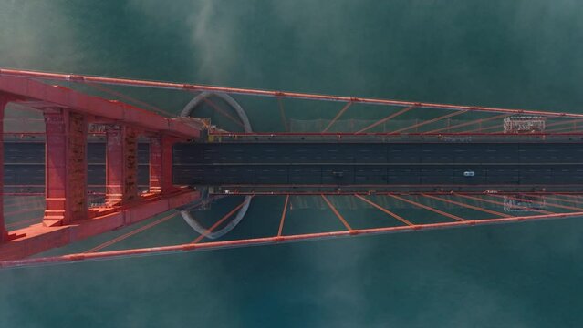 Cinematic top view of San Francisco in misty golden sunset light. View from top to bottom cars driving by road on tall red construction bridge of California landmark USA. Golden Gate Bridge overhead