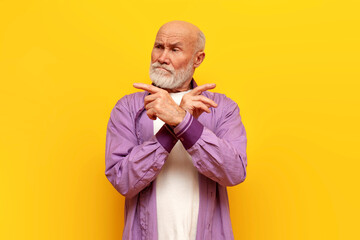unsure old bald grandfather with gray beard chooses and points on yellow isolated background