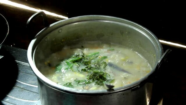 adding basil to the corn soup simmering in the pan