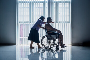 Overweight man sitting on a wheelchair being pushed by a female nurse