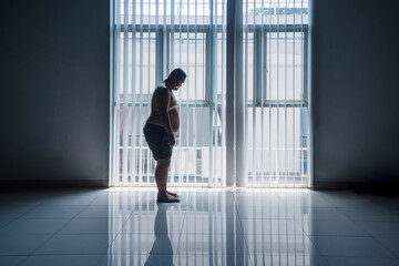 Asian 30s overweight man weighing himself with a scale